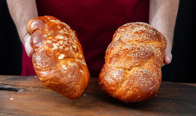 Easter sweet breads, baker hands holding two fresh baked  tsoureki braids over a wooden table