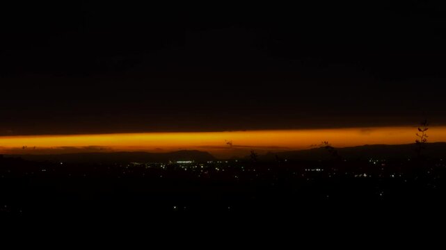 The sun is setting slowly on the horizon of hills and ocean in Auckland, New Zealand.