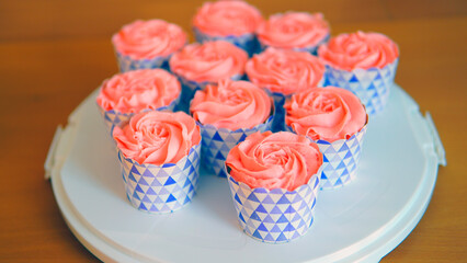 Close shot of many sweet cupcakes on the foreground while a baker decorating the last one