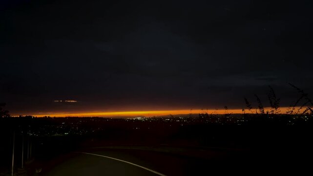 The sun is setting slowly on the horizon of hills and ocean in Auckland, New Zealand.