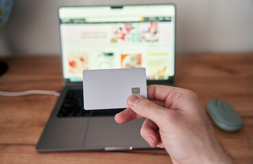 A person is holding a credit card in front of a personal computer with a laptop screen. They are using the touchpad to make a gesture