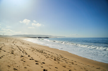 A tranquil beach scene shows soft footprints in warm sand, with gentle waves lapping at the inviting shore