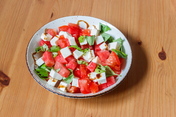 Fresh summer salad with watermelon, tomato, feta cheese and basil on wooden table