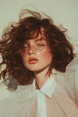 Trendy portrait of freckled woman with glitter makeup and wavy hair in soft lighting