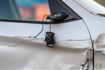 Badly crashed side and side mirror of a white car.
