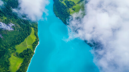Fototapeta premium Aerial View of Turquoise Lake Surrounded by Lush Green Landscape and Clouds