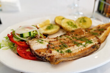 Grilled sole fish with potatoes and salad on white plate