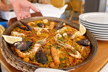 Waiter bringing delicious paella with shrimps and mussels in restaurant