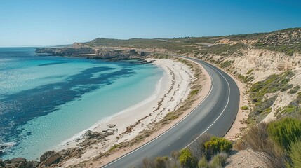 A scenic view of a rocky coastline with a winding highway perched above, overlooking a sandy beach and crystal-clear ocean waters.