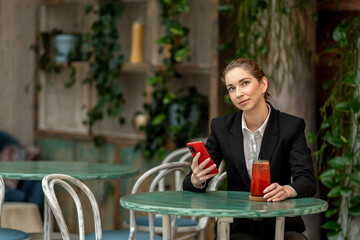 Businesswoman using smartphone and drinking juice in a cafe