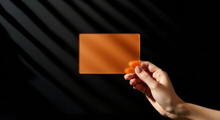 Hand holding an orange transparent card against a dark background