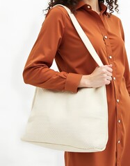 Woman in brown dress carrying a cream woven tote bag.  Stylish and practical everyday accessory.