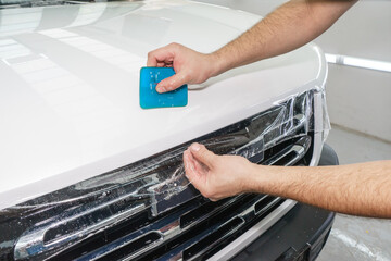 A worker is applying transparent film to a car to protect it from gravel and scratches on the hood of a white car. Applying transparent paint protection film