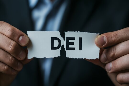 close up businessman tearing apart in half a rectangular piece of paper with bold text "DEI" End of DEI programs at corporates