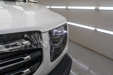 Fototapeta premium A worker is applying transparent film to a car to protect it from gravel and scratches on the hood of a white car. Applying transparent paint protection film