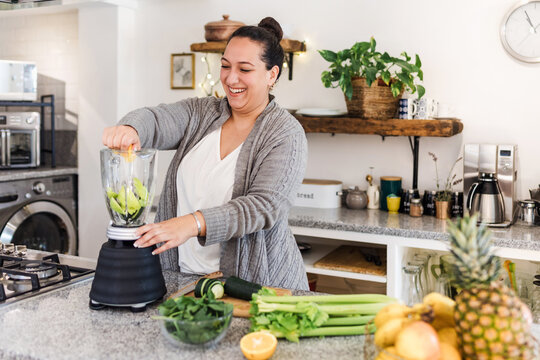 Hispanic woman overweight preparing detox or green juice in kitchen at home in Mexico Latin America, Mexican female plus size