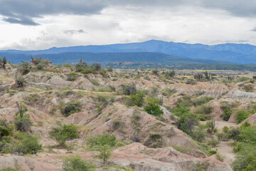 Panorama of the Tatacoa desert with a morning light. Typical geological formation coming from erosion. Cloudy day, green grass, mountains in the background. Villavieja, Huila, Colombia,