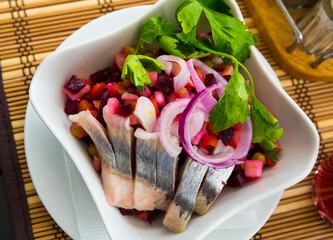 Traditional russian dish beetroot salad with herring on white plate