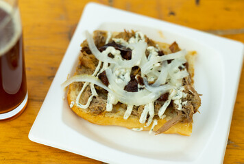 Sandwiches with lamb, sauce and onion served on white plate and glass of beer in cafe, fast food