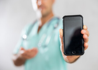 Adult man doctor in medical uniform posing with mobile phone in medical room