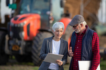 Farmer and business woman signing documents in front of tractor