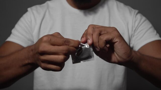 Man opening condom wrapper on gray background