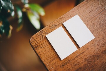 Two Blank White Cards On A Wooden Surface With Blurred Green Leaves In The Background
