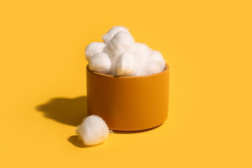 Bowl with cotton balls on yellow background