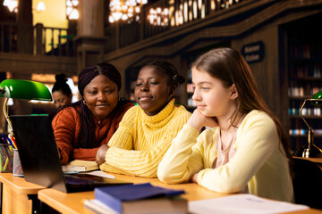 Two diverse children working with a tutor completing class notes in a library, helps with learning and tutoring for the school subjects. Professor ensures diversity and child development.