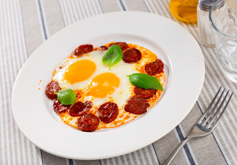 Homemade hearty breakfast - fried eggs with chorizo sausage. Dish is intricately decorated with slices of sausage, and complemented with bran bread.