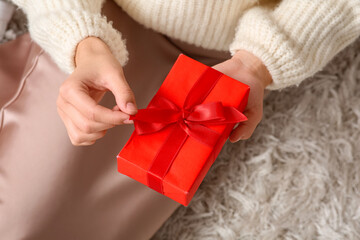 Young woman with gift box sitting on carpet at home, closeup. Valentine's Day celebration