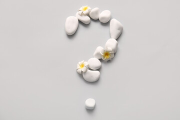 Question mark made of spa stones and tropical flowers on grey background