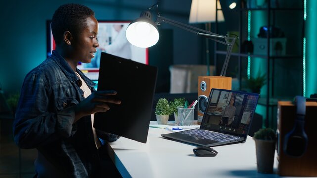 Manager talking with collaborator working from home, holding teleconference meeting to present project. Team leader talking with employee showing charts on clipboard during online videocall, camera A - Powered by Adobe