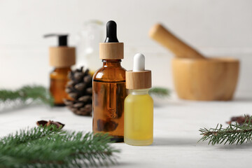 Bottles with coniferous cone essential oil on white wooden background