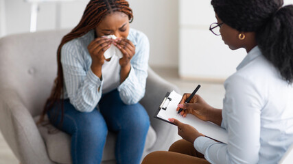 Unhappy black young woman crying at psychologist's office, panorama. Depressed millennial lady consulting psychiatrist, having session with counselor, dealing with negative emotions at clinic