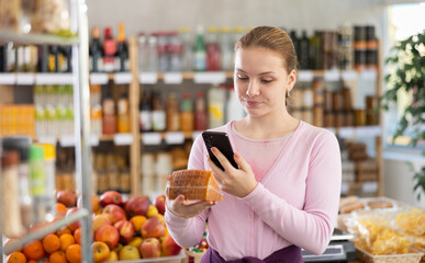 Young girl buyer scanning qr code for fresh cheese in grocery store