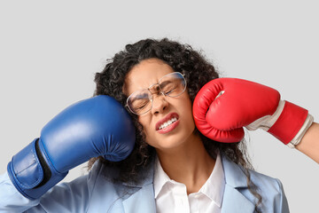 Young African-American businesswoman getting hit in her face with boxing gloves on light...