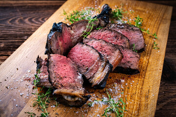 Traditional grilled barbecue dry aged tomahawk beef steak meat with salt and fresh herbs served and sliced as close-up on a wooden design board