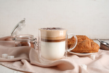 Glass cup of hot coffee and plate with tasty croissant on white background
