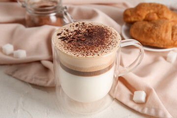 Glass cup of hot coffee and plate with tasty croissant on white background