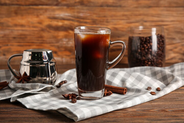 Glass cup of cold coffee with cinnamon and jug of fresh milk on wooden background