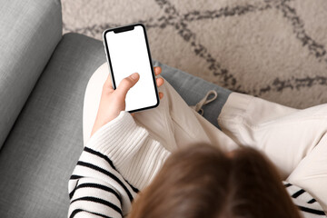 Young woman using blank mobile phone on sofa at home, top view