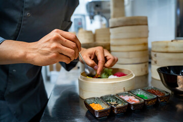 Chef preparing dumplings with toppings and condiments in a bamboo steamer - handmade food preparation in professional kitchen