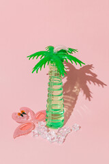 Summer creative layout with palm tree cocktail glass, flamingo party sunglasses and ice cubes against pastel pink background. Minimal beach cocktail party concept. Trendy summertime aesthetic idea.