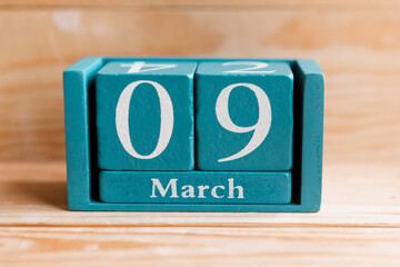 March 9. Blue cube calendar with month and date on wooden background.