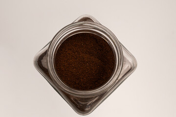 Top view of a glass jar with ground coffee inside on a white background. Detail shot of ground natural coffee in a transparent glass jar. Hand-ground coffee poured into a storage container.