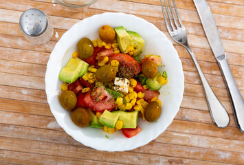 Fresh salad with olives, tomatoes, corn and cheese on a plate