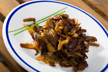 Golden fried mushrooms with onions served on white plate on wooden background..