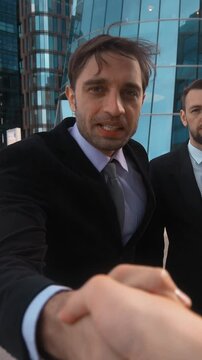 Young successful Businessman in formal suit recommed his confident collegue partner beard man in costume and tie to You. Modern glass business-centre building background. Teal and orange sunrise