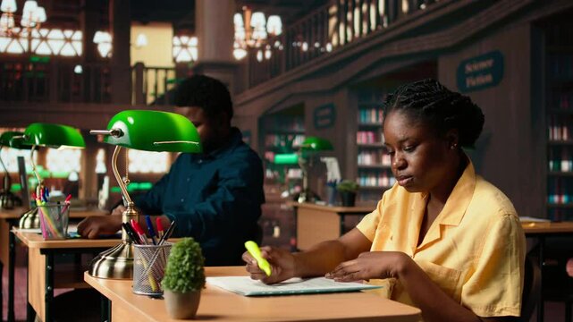 African american scholar highlighting the relevant information from class notes, creating a summary with highlighter pen. Student underlining key words and phrases from the course. Camera A.